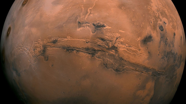 A continent-wide canyon reaches across the sand-red surface of Mars from space