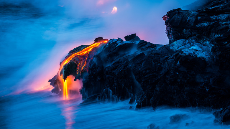 A time-lapse photo of lava streaming down a rock outcropping into the ocean