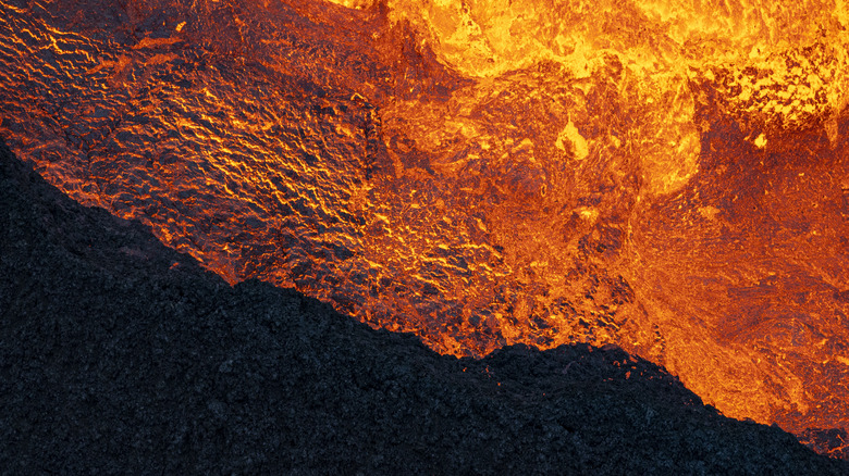 a bright orange and dark reddish lava flow with hardened black rock in the bottom left