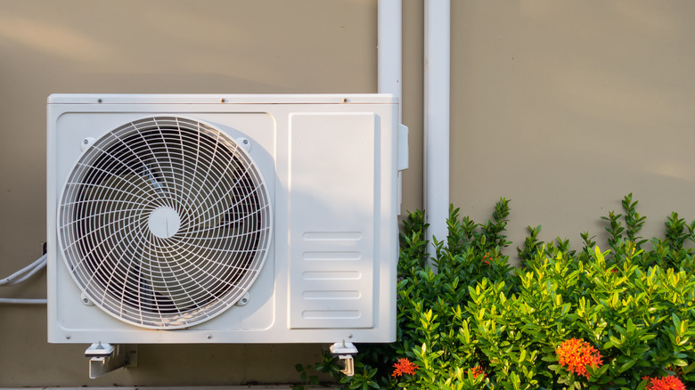 Outdoor condensing unit of an HVAC mounted to building next to plants