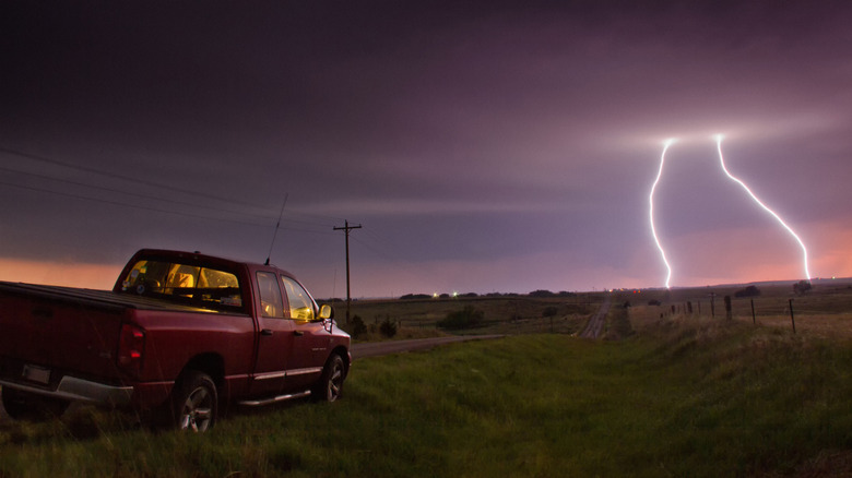 Red truck parked on side of road as lightning strikes in a field ahead