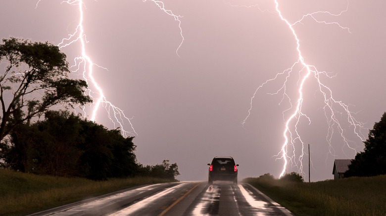 SUV reaches top of a hill as lightning strikes on both sides of the road