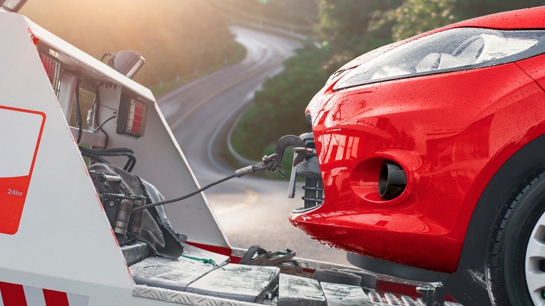 Close-up of red car's front end connected to a white tow truck after a rainstorm