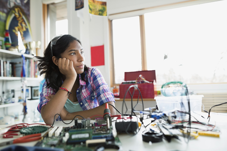 Pensive girl looking away assembling circuit board bedroom