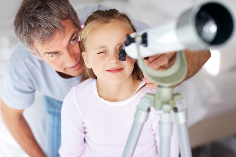 Adorable girl looking at sky through telescope with her father