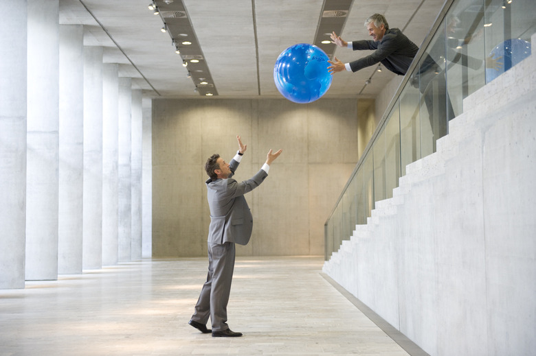 Businessmen throwing globe to each other in lobby