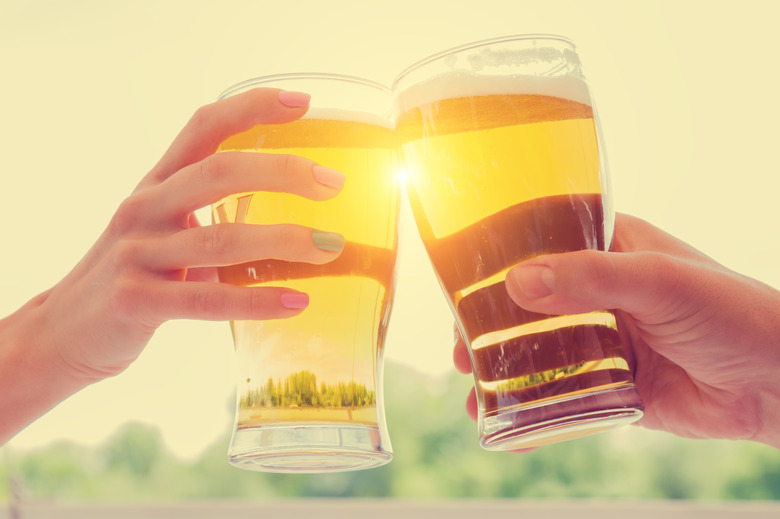 Hands holding two pints of beer in the sunlight