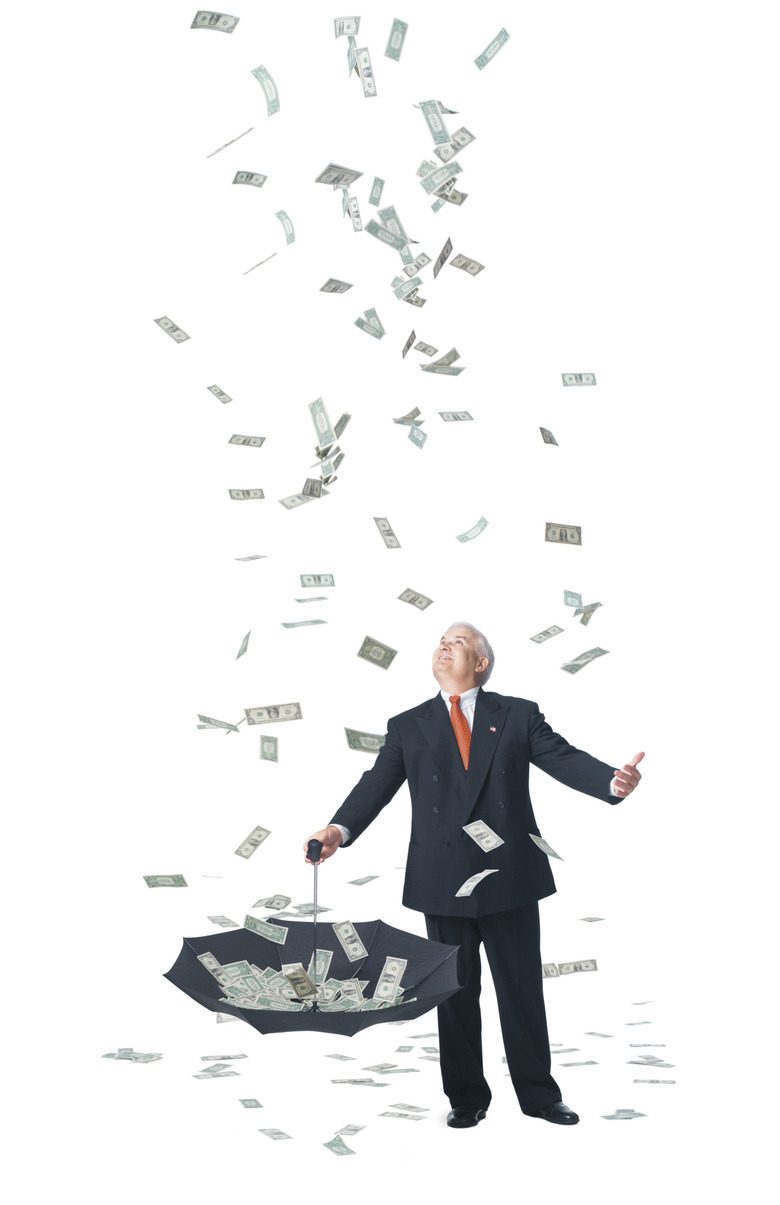 conceptual photo of a caucasian man in a suit standing in raining money and catches it in umbrella