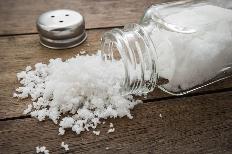 Spilled salt with salt shaker on wooden background