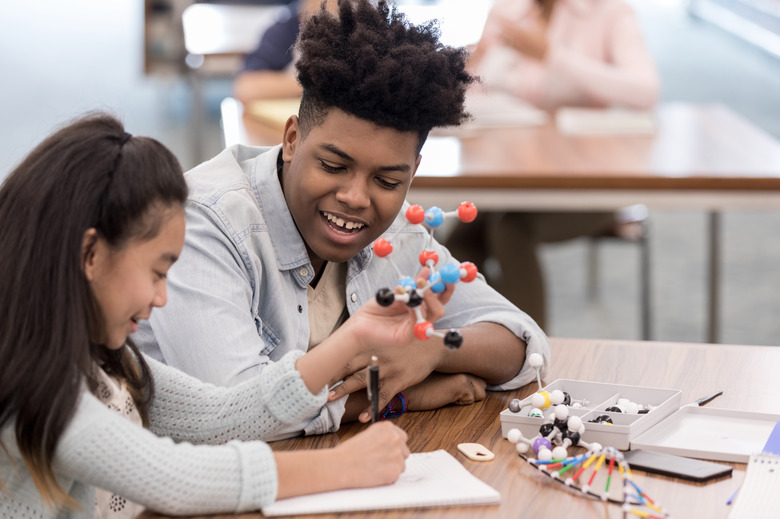 Girl draws molecule while teen helps