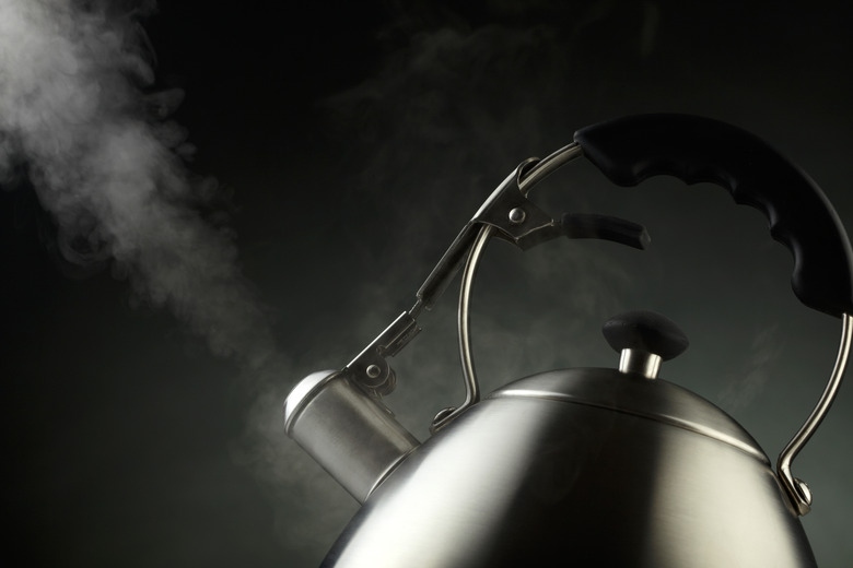 Tea kettle with boiling water over dark background