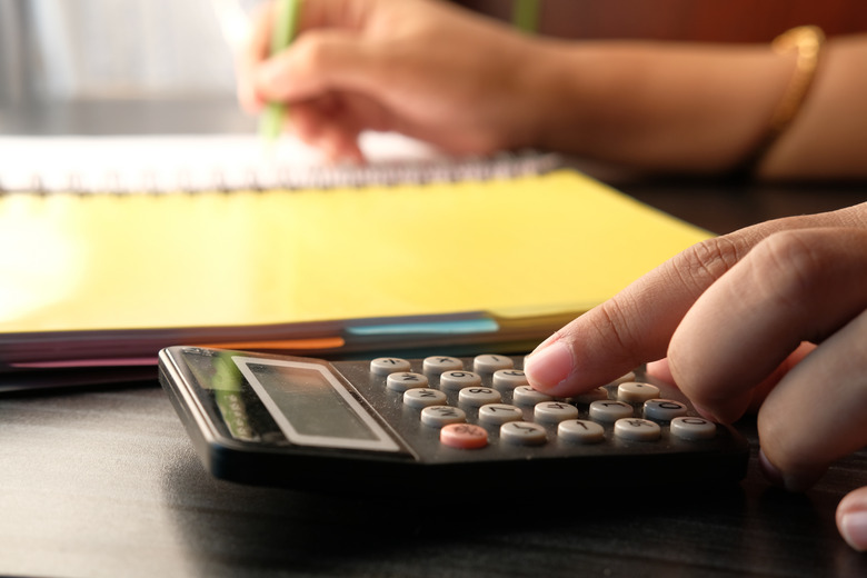 finger of girl presses on button of black calculator on table