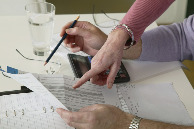 Mature woman pointing to bill held by mature man at desk, close-up