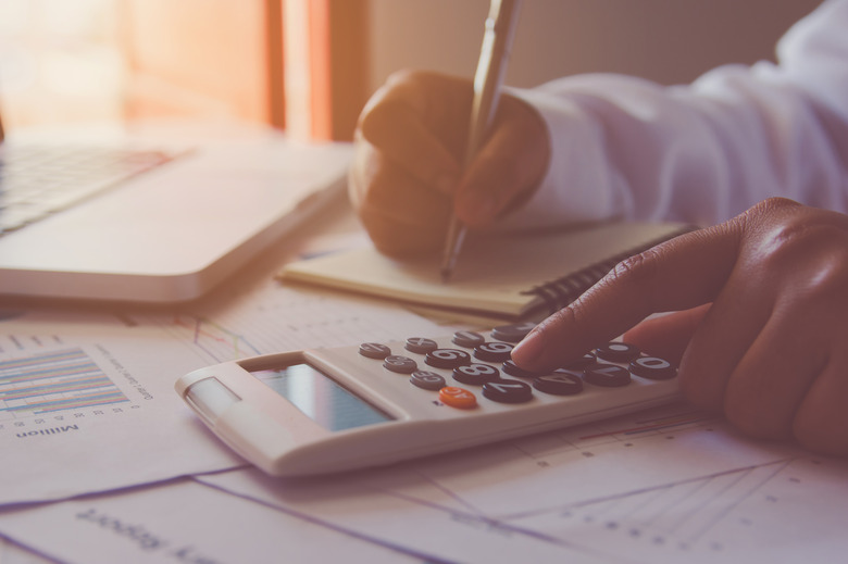 Man hand using a financial calculator with writing make note and Financial data analyzing on desk at home