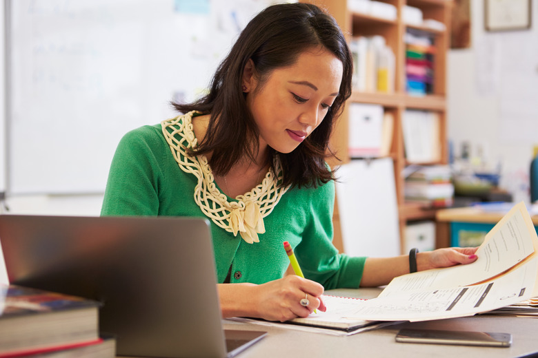 Female Asian teacher at her desk marking studentsâ work