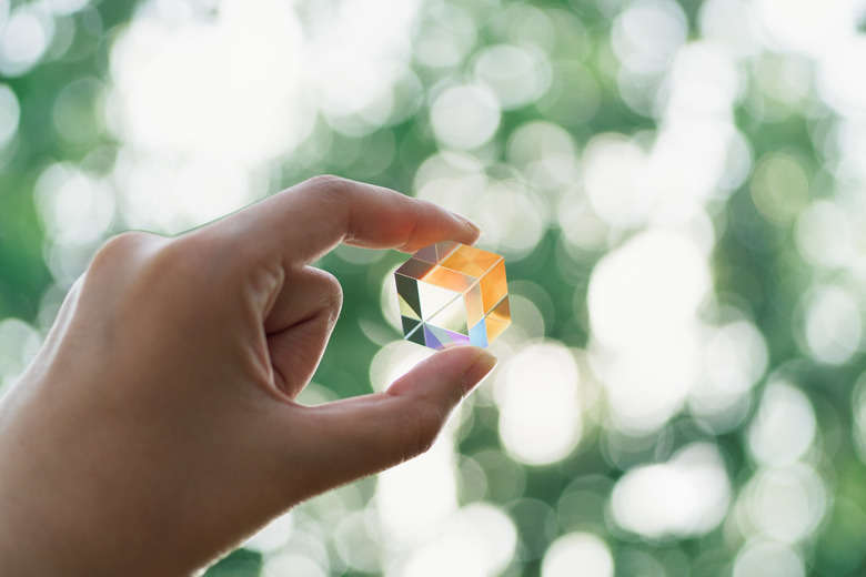 Hand Holding Cube Prism Against Green Trees Bokeh