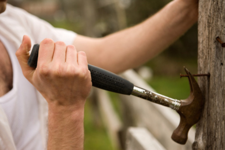 A man pulling an old, rusty nail out of a fence post with a hammer