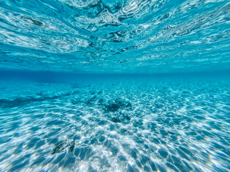 Underneath a wave in the clear ocean waters looking at rocks and shells on the ocean floor and natural water patterns