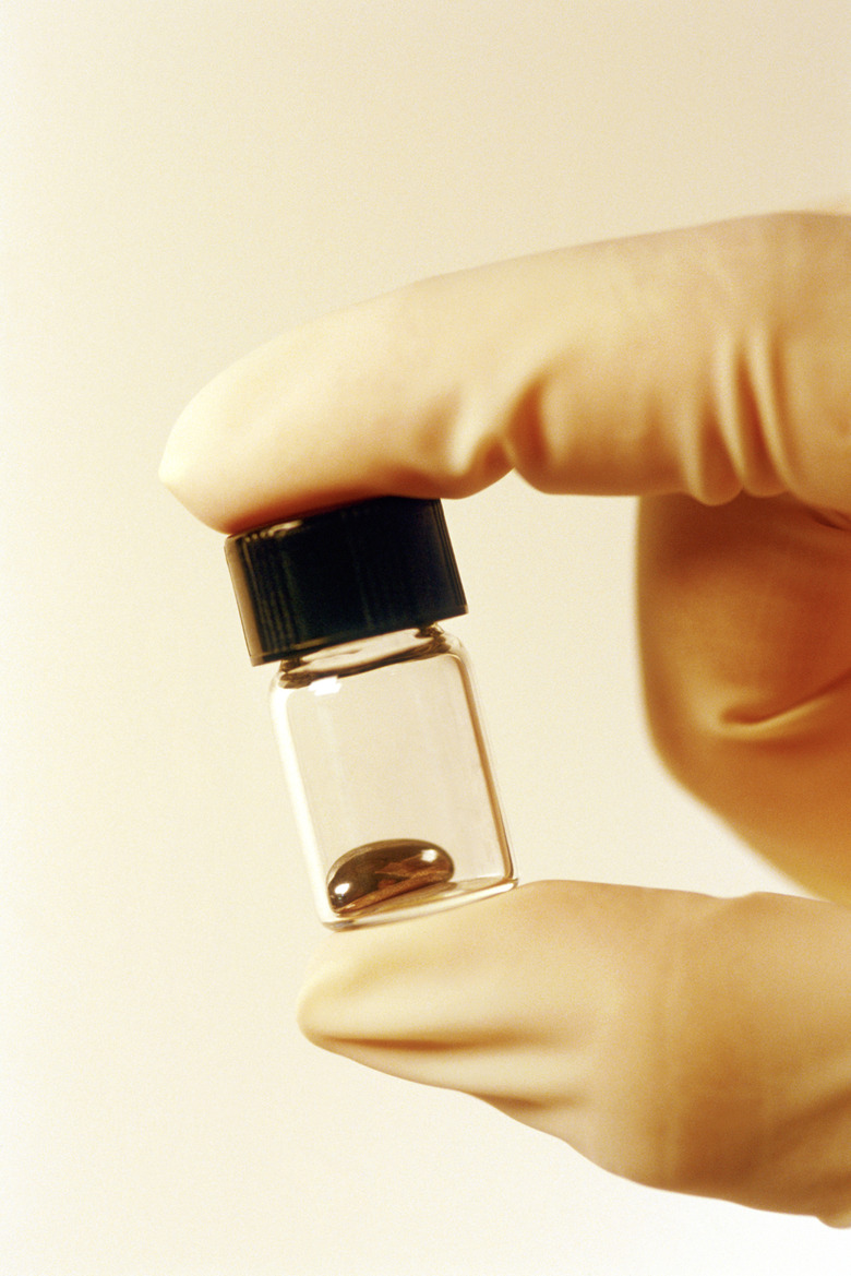 Hand in rubber glove holding mercury in a small jar