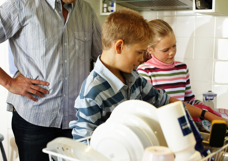 Father standing behind twins (10-12) washing and wiping up at kitchen sink, close-up