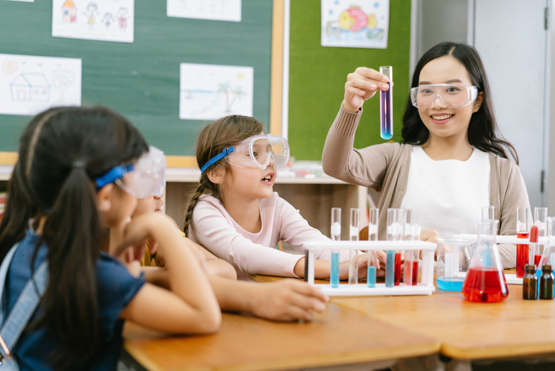 Group of little pupils with female teacher making experiment in science class.