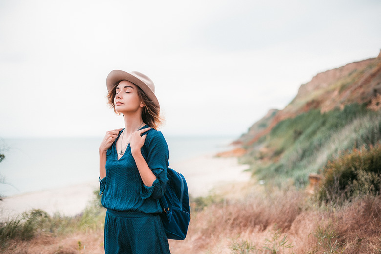 Mid adult woman in coastal setting, carrying backpack, breathing in fresh air