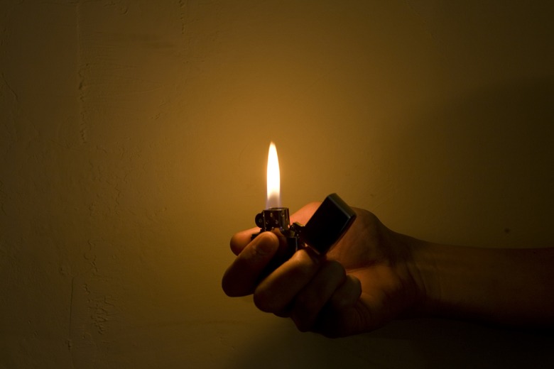 A Hand Holding a Cigarette Lighter and Illuminating the Darkness