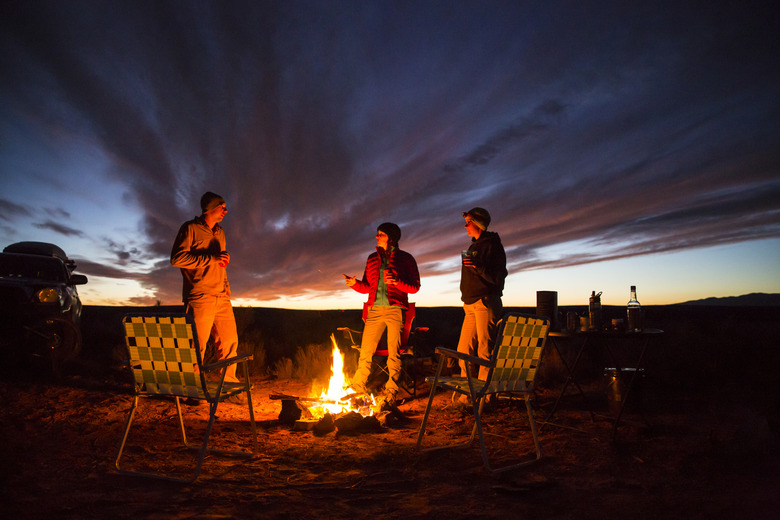 Three friends handing out at a campfire.