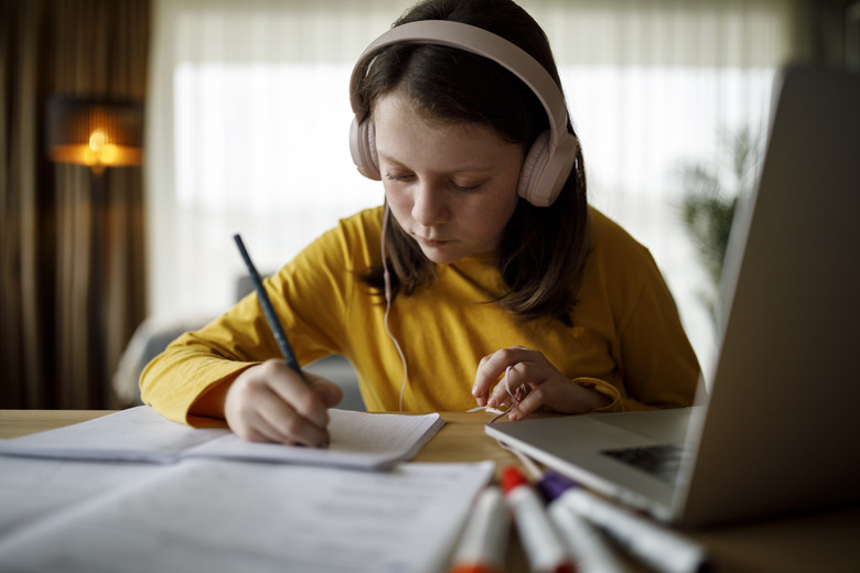 Young school girl with headphones using laptop for studying at home