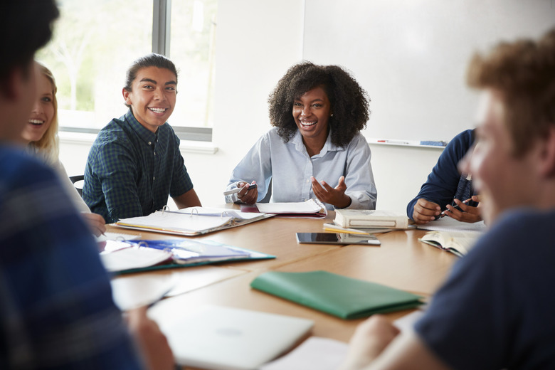 Female High School Tutor Sitting At Table With Pupils Teaching Maths Class