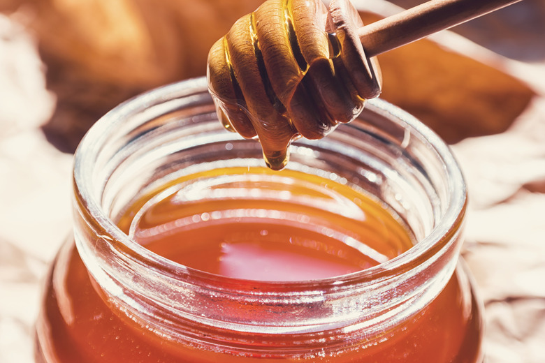 Honey runs from a dipper in to a glass of jar