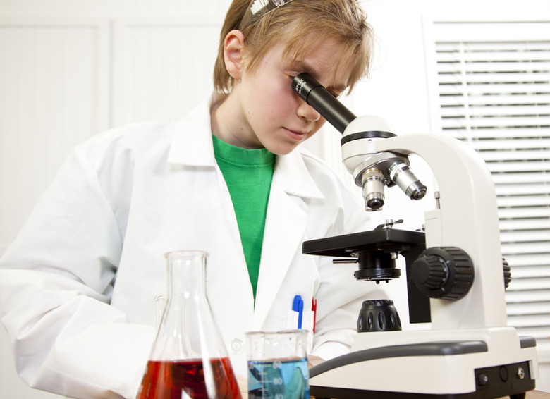 Pre-teen scientist wearing lab coat looking into microscope