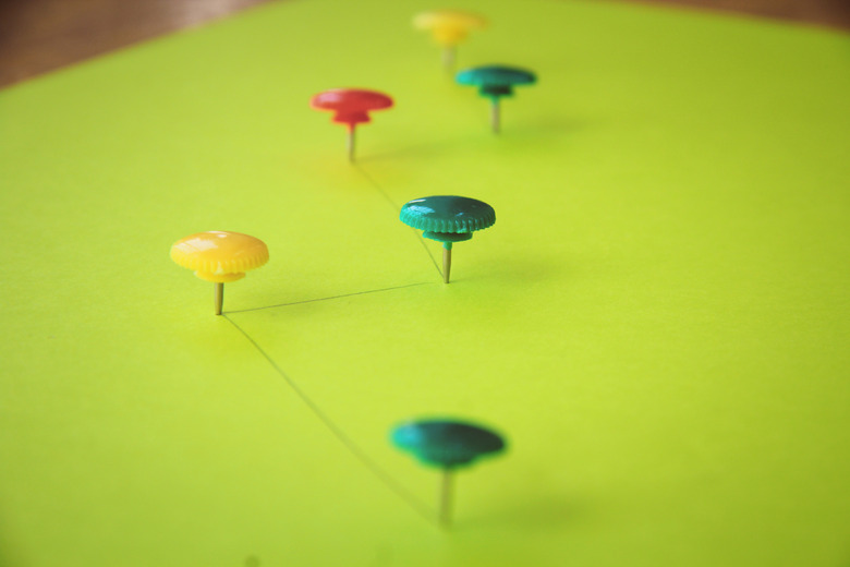 Colorful push pins on green paper.