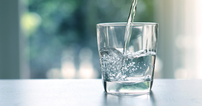 Close up of pouring purified fresh drinking water into a glass on a table