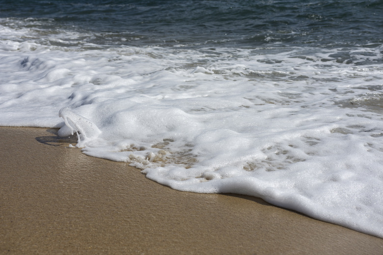 Wave with foam on sandy Mediterranean beach. Close up view. Selective focus. Copy, negative space. Natural texture background