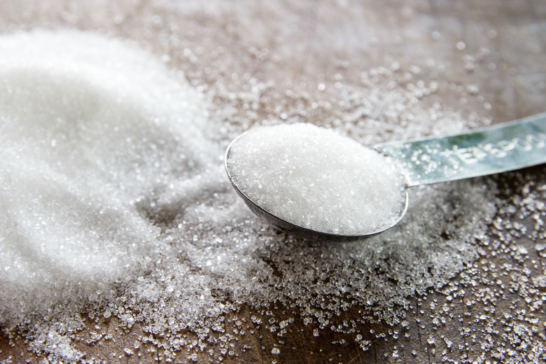 granulated sugar in spoon and sugar pile on wooden