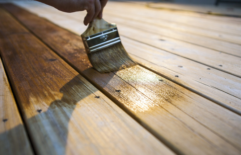 Male Carpenter Applying Varnish To Wooden Deck