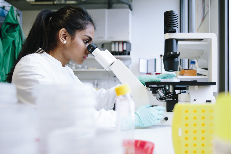 Young female scientist watching through microscope in laboratory