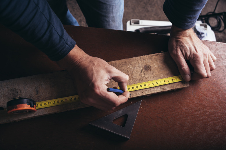 Amateur carpenter measures the board with the meter tape