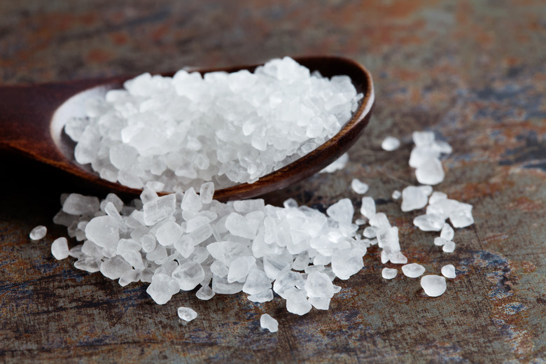 Sea salt condiment macro view. Natural mineral flavoring food preservative, Saline sodium chloride white crystal in wooden spoon, aged background. Shallow depth field