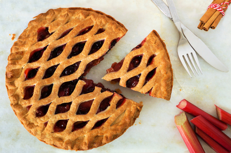 Strawberry and rhubarb pie with slice on marble background