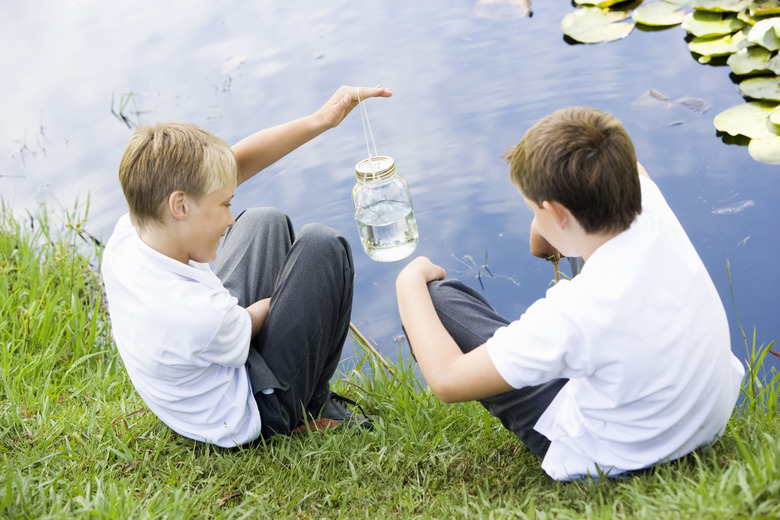 Children holding jar of water by lake