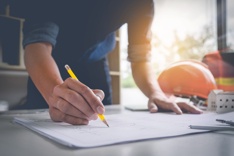 Architect man holding pencil working with laptop and blueprints for architectural plan, engineer sketching a construction project concept.