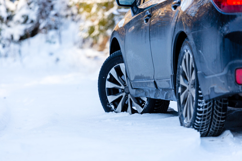 Winter tires. Black SUV car rear view on snowy forest road. Winter conditions.