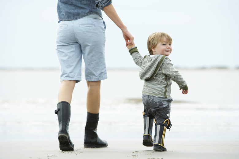 Mother and son (15-18 months) walking on beach, rear view