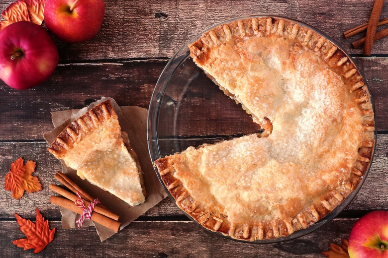 Apple pie, overhead scene with cut slice on rustic wood