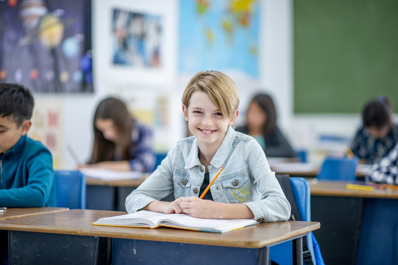 Elementary Girl With Textbook Open on Her Desk Writing stock photo