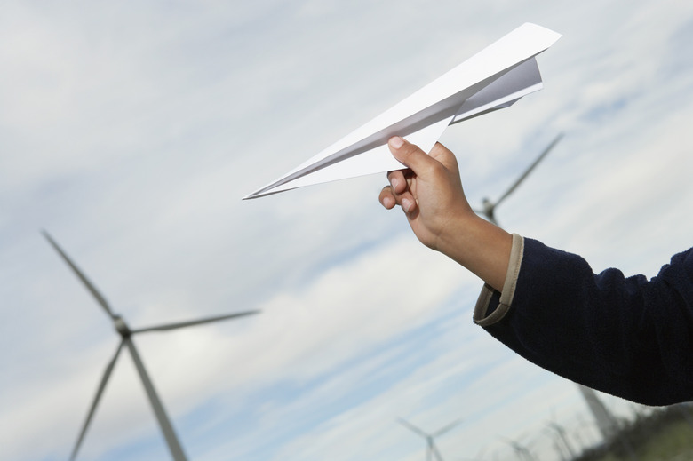 Boys hand throwing paper plane at wind farm, close-up