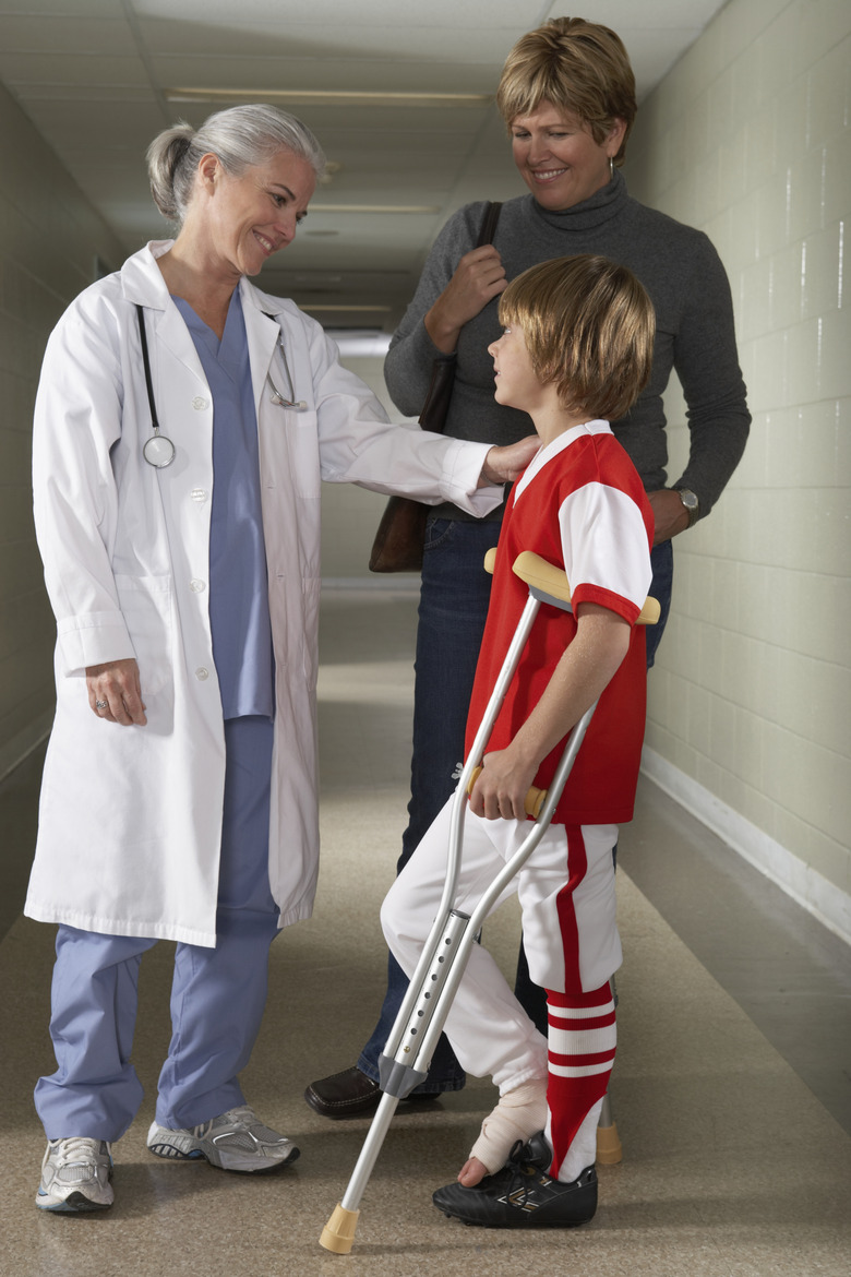 Doctor with boy (10-11) using crutches, standing in corridor, smiling