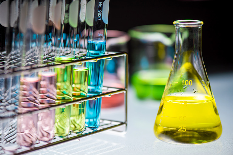 Yellow chemical liquid containing in flask with lab glassware on black background, la research and development concept.